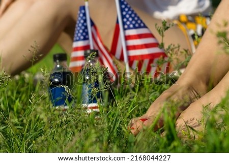 Woman legs and USA flags with soda bottles on grass lawn, celebration of patriotic american national holiday 4th of july independence day, festive picnic in park, faceless concept
