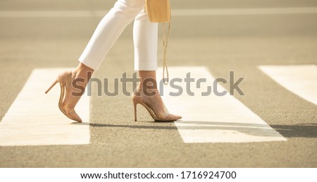 Сlose up of woman legs walking on crosswalk. The woman is wearing shoes on high heels. Handbag in woman hand.