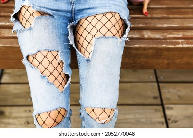 woman legs wearing ripped jeans and fishnet pantyhose close up. girl wearing torn jeans and fishnet tights close up outdoors. fishnet tights stick out from under torn jeans. 