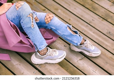woman legs wearing ripped jeans and fishnet pantyhose close up. girl wearing torn jeans and fishnet tights close up outdoors. fishnet tights stick out from under torn jeans.