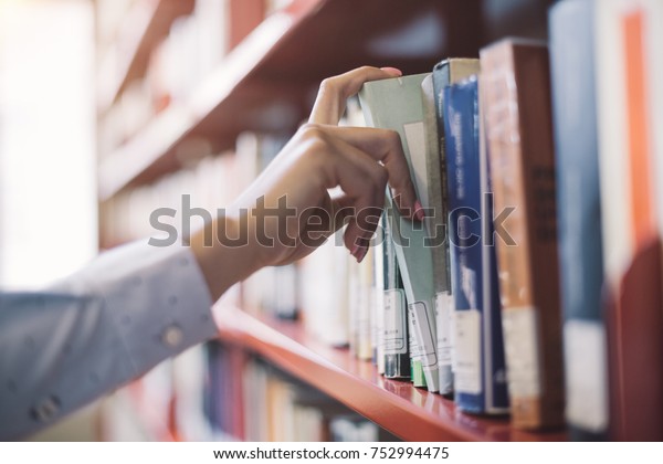 Woman at the library, she is\
searching books on the bookshelf and picking a textbook, hand close\
up