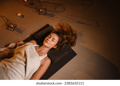 A woman lies on the floor covered with a blanket with her eyes closed and relaxes after a workout , shavasana pose. - Powered by Shutterstock