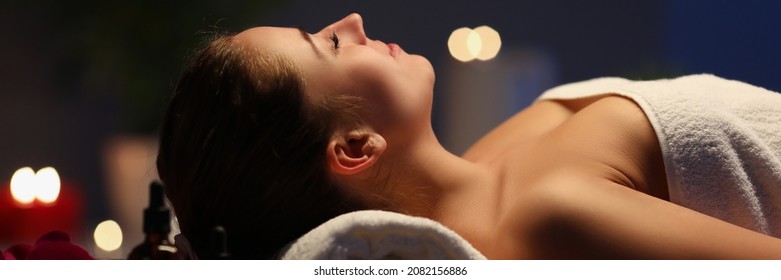 Woman Lies On Massage Table In Dark Spa Room