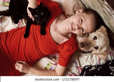 A Woman Lies On A Sofa With A Cat And A Dog. Love For Pets Concept.