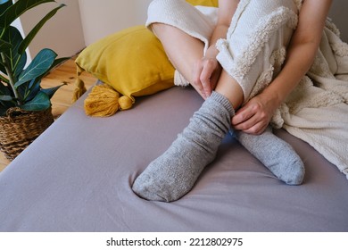 The woman lies in warm gray socks in bed and covers herself with a blanket. Women's legs in cozy socks. View from above. Warm evenings at home - Shutterstock ID 2212802975
