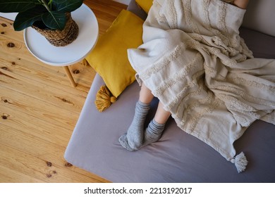 The Woman Lies In Warm Gray Socks In Bed And Covers Herself With A Blanket. Women's Legs In Cozy Socks. View From Above. Warm Evenings At Home