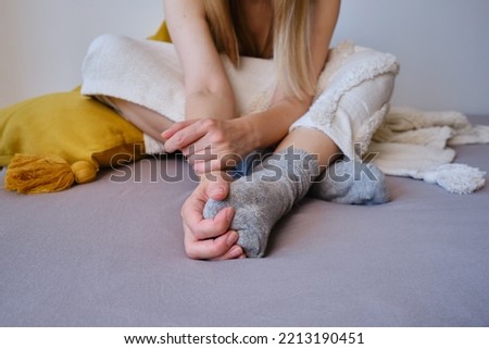 The woman lies in warm gray socks in bed and covers herself with a blanket. Women's legs in cozy socks. View from above. Warm evenings at home