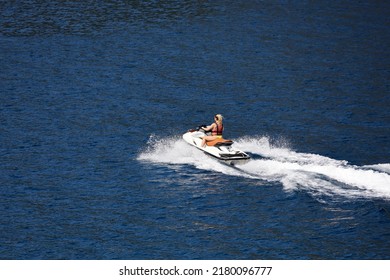 Woman In Life Vest And Swimsuit Rides A Jet Ski On The Sea. Water Sport In Summer, Riding A Hydrocycle