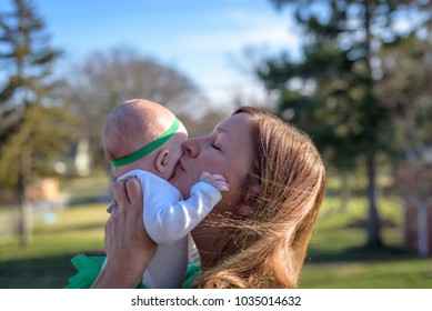 woman lifting baby up in air to kiss outside on St. Patrick's Day