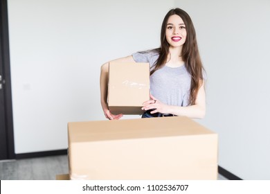 Woman Lifting Cardboard Box While Moving Home, Smiling.