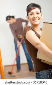 Woman Lifting Cardboard Box While Moving Home, Smiling.