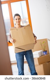 Woman Lifting Cardboard Box While Moving Home, Smiling.