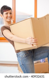 Woman Lifting Cardboard Box While Moving Home, Smiling.