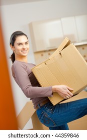 Woman Lifting Cardboard Box While Moving Home, Smiling.