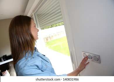 Woman Lifting Electric Shutters In House