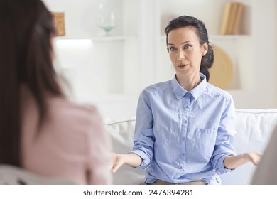 A woman in a light blue shirt is engaging in a counseling session during daytime in a cozy, well-lit office with white walls and minimal decor. She appears attentive and expressive - Powered by Shutterstock