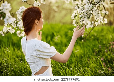 a woman in a light dress sits with her back to the camera near a flowering apple tree - Shutterstock ID 2279799691