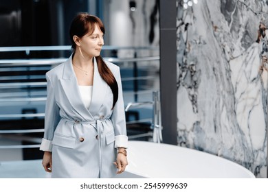 A woman in a light grey suit stands in a modern showroom, looking towards the right side of the frame. A large, white, freestanding bathtub is in the foreground.  - Powered by Shutterstock