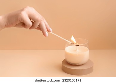 Woman lighting candle on pale orange background
