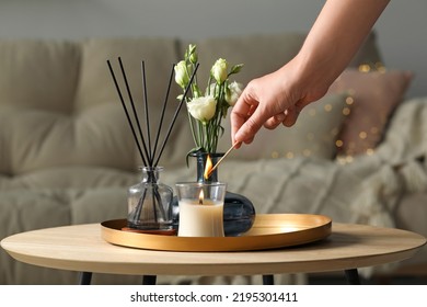 Woman lighting candle at wooden table in living room, closeup