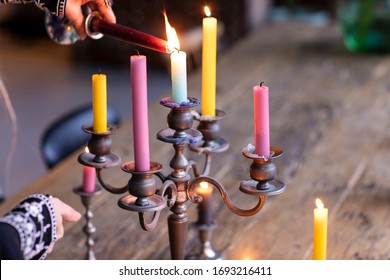 A woman lighting different coloured candles in a vintage metal candle holder to create a nice atmosphere in her home. An Eclectic styled living with a wooden rustic table and warm colours, decoration