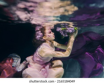 Woman With Lilac Bouquet In Colorful Clothes On The Dark Background Swimming Underwater