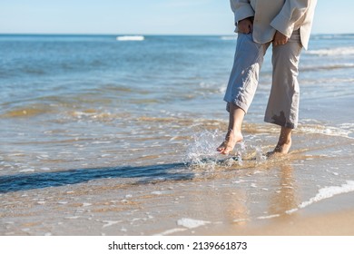 Woman In Linen Trousers Walking Barefoot On Sandy Beach