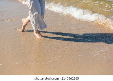 Woman In Linen Trousers Walking Barefoot On Sandy Beach