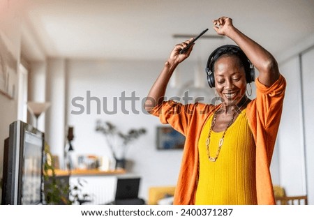 Woman listening to music with headphones connected to her smartphone in the living room at home
