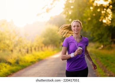 Woman listening to music on her earplugs and MP3 player while jogging along a country road in a healthy lifestyle, exercise and fitness concept - Powered by Shutterstock