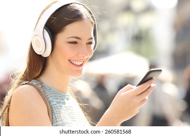 Woman listening wireless music with headphones from a smart phone in the street