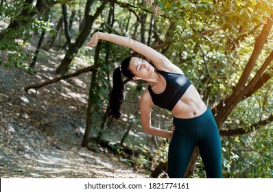 A woman listens to music in headphones and does a warm-up before jogging and active sports. Beautiful girl goes in for sports in the summer in the forest. - Shutterstock ID 1821774161