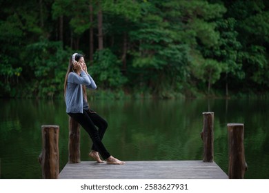 Woman listens to music via Bluetooth headphones, enjoying the peaceful lakeside view.