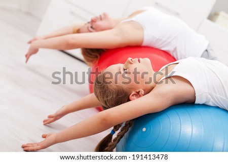 Woman and little girl exercising - stretching on large gymnastic balls, closeup