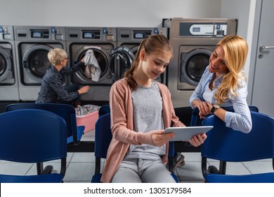 Woman And Little Girl Using Technology While Waiting To Laundry Done At Laundromat