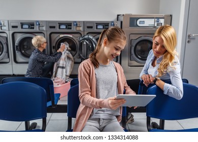 Woman And Little Girl Using Technology While Waiting To Laundry Done At Laundromat