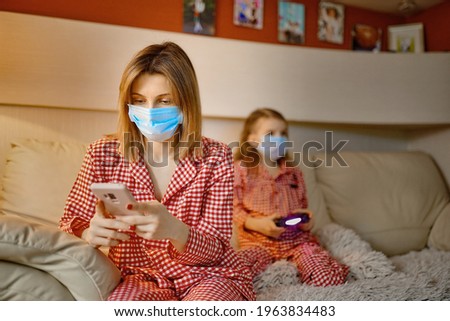 Woman with Little kid at home isolation auto quarantine wearing face mask with smart phone for reading information about COVID-19.