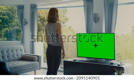 Woman in living room stands infront of Green Screen TV