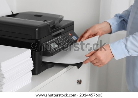 Woman loading paper into printer at white chest of drawers indoors, closeup