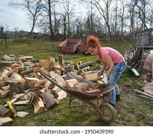 Woman loading split wood in the wheelbarrow to transport it to the shed - Powered by Shutterstock