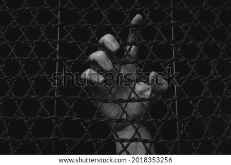 Woman Locked Up and Trapped in Captivity in the Dark with Hand Gripping the Cage