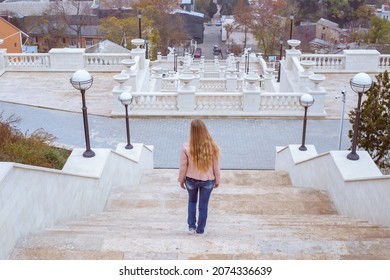 A Woman With Long Blond Hair Descends A High White Staircase In The Crimea In Kerch. Observation Deck. Travel And Tourism.