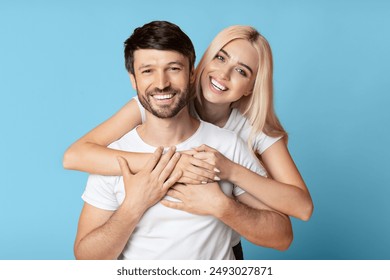 A woman with long, blonde hair is embracing a man from behind. Both are smiling brightly at the camera. They are wearing simple white t-shirts and appear to be enjoying each other's company - Powered by Shutterstock