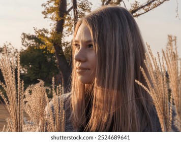 A woman with long, blonde hair stands in a field of tall grass, looking off to the side - Powered by Shutterstock