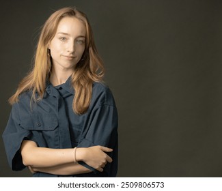 A woman with long blonde hair wearing a loose blue shirt is posing with a serious expression in a professional studio setting with a dark grey background. - Powered by Shutterstock