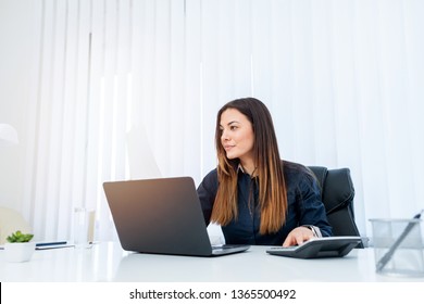 Woman With Long Brown Hair Sitting Behind Her Office Desk And Calculating Income.