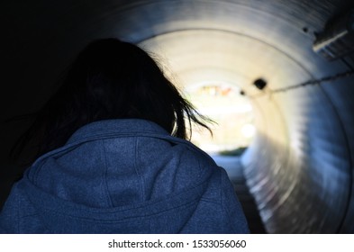 Woman with long brown hair wearing a sweater walking in a small tunnel - Powered by Shutterstock