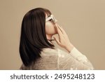 Woman, long brown hair, white shirt, glasses a woman with long brown hair, wearing a white shirt and glasses, looks up at the sky with her hand on her chin and eyes closed, deep in thought or