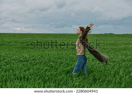 a woman in a long coat stands in tall green grass in a field, in cloudy weather, enjoying nature and the view