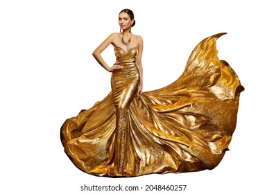 Woman In Long Golden Evening Dress Waving In Air. Elegant Fashion Model In Shiny Luxury Gown With Gold Jewelry Over Studio White Background